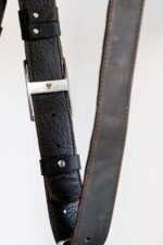 Close-up of an adjustable dark leather camera harness strap with metal buckle and stitched edges.