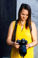 Woman wearing a dark leather camera harness while looking down at a camera in her hands.