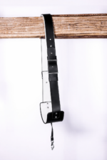 Black and white leather camera strap with white padded underside, adjustable buckle, stitched edges, and silver clasp hardware hanging from a rustic wooden beam on a light gray background.