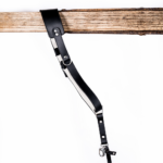 Black and white leather camera strap with white padded underside, silver rivets, metal rings, adjustable strap holes, and clasp hardware hanging from a rustic wooden beam on a light gray background.