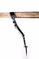 Black and white leather camera strap with white padded underside, silver rivets, metal rings, adjustable strap holes, and clasp hardware hanging from a rustic wooden beam on a light gray background.