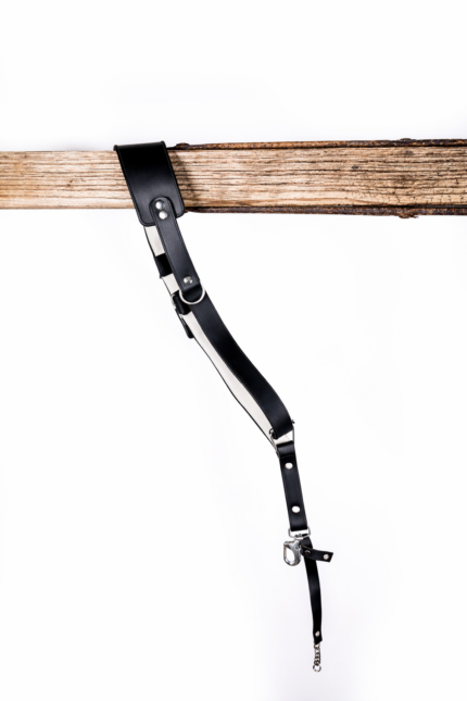 Black and white leather camera strap with white padded underside, silver rivets, metal rings, adjustable strap holes, and clasp hardware hanging from a rustic wooden beam on a light gray background.