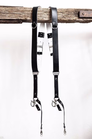 Black GenuineStrap SW Edition leather camera strap with white inner padding, showing D-ring ends hanging over wooden beam