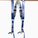 Complete front view of Blue Shanty leather camera harness showing dual royal blue shoulder straps with metal D-rings, grey and navy layered center strap, adjustable leather segments, and metal carabiner clips at lower attachment points