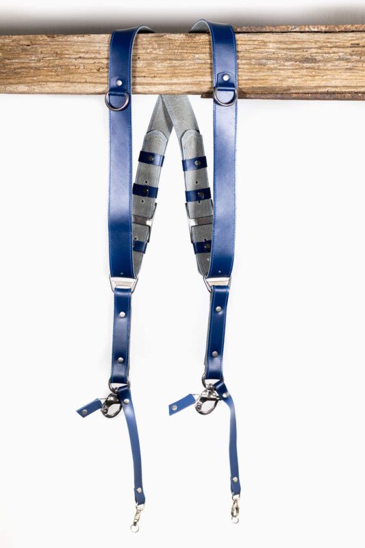 Complete front view of Blue Shanty leather camera harness showing dual royal blue shoulder straps with metal D-rings, grey and navy layered center strap, adjustable leather segments, and metal carabiner clips at lower attachment points