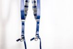 Full display of Blue Shanty camera harness showing complete X-design with metal connectors, adjustable leather segments on center strap, white stitching throughout, and dual carabiner attachments at base