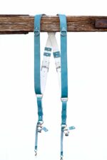 Full display of Blue Sirocco leather camera harness showing complete X-design with turquoise shoulder straps, white center X-strap with teal leather accent patches, metal square connectors, adjustable leather segments, and dual metal carabiner clips with leather tags