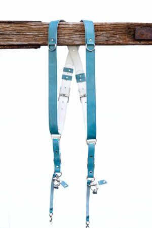 Full display of Blue Sirocco leather camera harness showing complete X-design with turquoise shoulder straps, white center X-strap with teal leather accent patches, metal square connectors, adjustable leather segments, and dual metal carabiner clips with leather tags