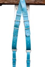 Blue Sirocco leather camera harness displayed overhead on weathered wood beam, showing full X-harness design with turquoise leather shoulder straps, white center strap with teal accent bands, metal square connectors, and white stitching throughout