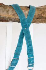 Center X-strap detail of Blue Vintage harness showing teal vintage leather with white stitching, white-trimmed metal square connectors, layered teal and navy accent bands with rivet detail
