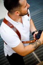 close-up of a dark brown leather dual camera harness worn across the chest with a camera attached.