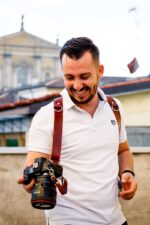 Man smiling with a camera while wearing a dark brown leather dual camera harness outdoors