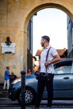 Man wearing a dark brown leather dual camera harness while walking outdoors with a camera.