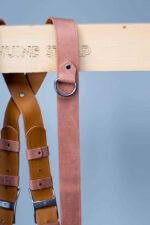 Brown Siena camera harness positioned in wooden presentation box, showing tan leather shoulder straps with metal D-rings, rich brown center strap with metal square connectors and adjustable leather bands