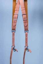 Full display of Brown Siena leather camera harness on aged wood showing complete X-design with golden-brown shoulder straps with metal D-rings, caramel-toned center strap with multiple adjustable leather accent bands, metal square connectors, and carabiner clips with leather attachment tags