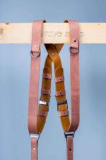 Center X-strap detail of Brown Siena harness on weathered wood, showing warm caramel brown leather with layered tan accent bands, metal square connectors, white rivets, and stitched construction