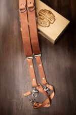 Brown Siena leather camera harness laid flat with branded wooden presentation box, showing dual tan leather shoulder straps with metal D-rings, brown center strap, and metal carabiner attachments with leather tags