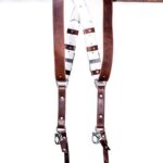 Brown Vintage White Padding leather camera harness displayed on weathered wood beam, showing full X-harness design with brown leather shoulder straps, white padded center strap with brown leather accent bands, metal D-ring connectors, and carabiner clips