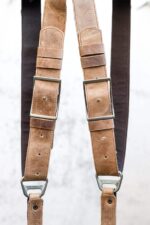 Close-up of Brown Wild West Vintage harness shoulder straps showing tan vintage leather with patina, adjustable brown leather accent bands with metal square connectors, white stitch detailing, and riveted construction