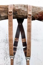 Detail view of Brown Wild West Vintage harness showing tan shoulder straps with metal D-rings, black center strap with tiered brown leather accent bands, metal square connectors, and riveted leather segments