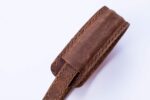 Brown leather strap close-up showing folded keeper and stitched reinforcement.