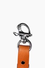 Leather camera harness slider kit in tan leather with metal clasp clip, close-up on white background