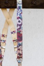 Detail of the upper crossback area showing the cream leather padding crossing beneath a dark wooden beam, with the floral printed strap running alongside, branded eagle-logo silver buckles, and floral leather keeper loops.