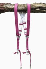 Fuchsia candy leather dual camera harness hanging from a rustic wooden branch against a white background, showing the full front view with two pebbled leather shoulder straps, white leather back panel with leather keepers, silver adjustable buckles, snap shackle clips, and lobster claw clasps at each end.