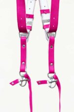 Close-up detail of the lower section of the fuchsia candy leather camera harness showing both strap ends with branded "GENUINESTRAP" metal connectors, white leather backing, silver rivets, D-rings, snap shackle clips, and leather safety tethers.