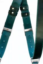 Detail shot of Green Amulet harness center X-strap showing darker upper leather transitioning to teal, with black leather adjustment bands and white rivets