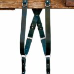 Green Amulet leather camera harness showing dual-tone teal and dark green leather, full X-harness design with adjustable segments and metal connectors over wooden beam