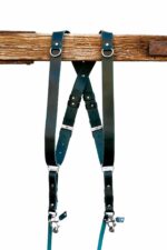 Green Amulet leather camera harness showing dual-tone teal and dark green leather, full X-harness design with adjustable segments and metal connectors over wooden beam