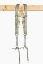 Full-length front view of the Green Marble leather dual camera harness hanging from the "Genuine Strap" branded wooden beam, showing the complete harness with cream leather crossback, marbled sage-green straps, silver buckles, D-rings, triangular connectors, and snap-hook camera attachments with green leather safety tabs at the bottom.