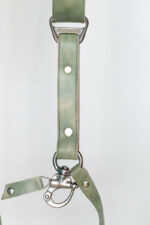 Close-up detail of a single strap end showing the "GENUINESTRAP" branded triangular D-ring connector, marbled sage-green leather with silver rivets, O-ring, and marine-grade snap hook with a matching green leather safety tab.