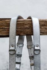 Front view of Grey Flower Embossed harness showing dual silver shoulder straps with ornate embossed flower pattern throughout, light center X-strap with matching floral embossing, darker grey layered accent bands, and metal D-rings with engraved connectors