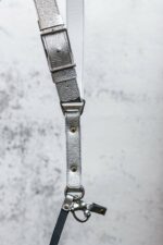 Close-up detail of Grey Flower Embossed harness center strap showing embossed flower pattern, ombre color gradient from light silver to darker grey, metal square connector, rivets, and leather overlay band