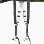 Grey goose vintage leather dual camera harness hanging from a rustic wooden branch against a white background, showing the full front view with two shoulder straps, a white leather back panel with leather keepers, adjustable silver buckles, riveted construction, and snap shackle clips with lobster claw clasps at each end.