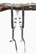 Grey goose vintage leather dual camera harness hanging from a rustic wooden branch against a white background, showing the full front view with two shoulder straps, a white leather back panel with leather keepers, adjustable silver buckles, riveted construction, and snap shackle clips with lobster claw clasps at each end.