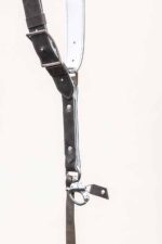 Detail shot of a single strap junction on the grey goose vintage leather camera harness, showing the silver adjustable buckle, white leather backing, riveted construction, D-ring, snap shackle clip, and leather safety tether against a light background.
