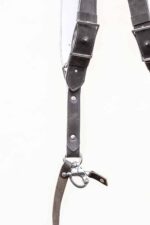 Close-up detail of the lower section of the grey goose leather camera harness showing the adjustable buckle area, riveted leather strap with contrast stitching, D-ring, and snap shackle clip with leather safety tether against a white background.