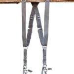 Grey Sandstone leather camera harness displayed on wooden beam showing full X-harness design with dual shoulder straps, adjustable leather segments, and metal D-rings