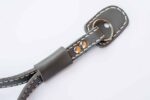 Close-up of a grey leather strap end with metal ring connector and stitching.