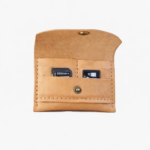 Light brown leather battery and SD card holder opened to show storage slots with memory cards inside on a light gray background.