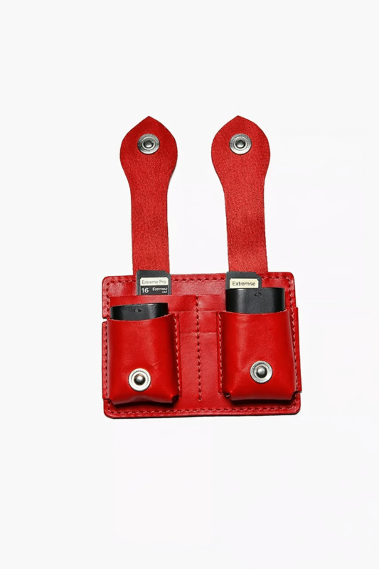 Red leather dual battery holder with two hanging tabs on a light background.