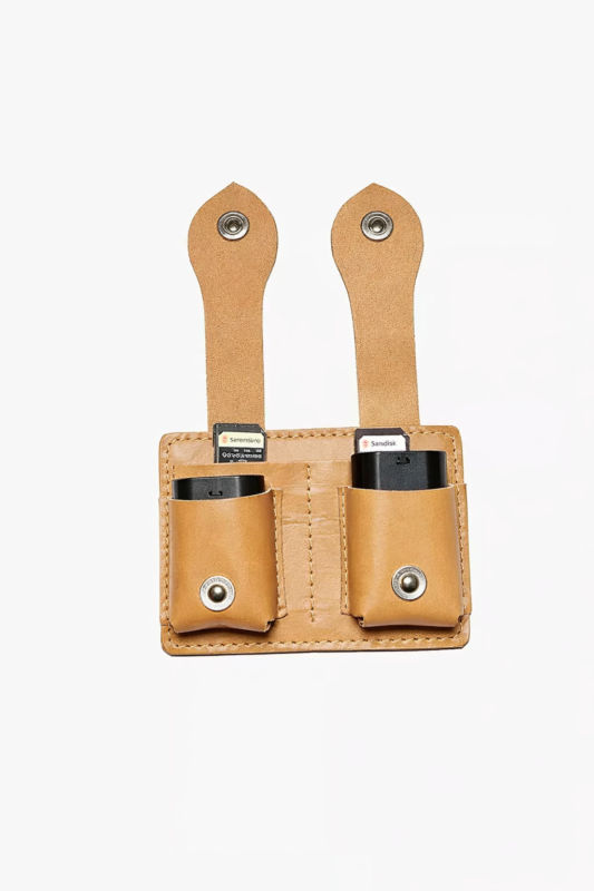 Light brown leather dual battery holder with two hanging tabs on a light background.