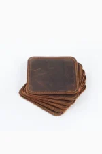A stack of six square dark brown leather coasters with rounded corners and tan contrast edge stitching, viewed from above on a white background.