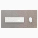 Top-down view of a light gray leather desk mat with stitched edges on a white background, with a white full-size wireless keyboard centered on the left and a white wireless mouse on the right.