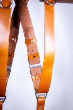 Close-up detail of Light Brown Garioch harness center X-strap showing layered leather segments transitioning from brown to orange with metal hardware and rivets