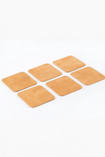 Set of six light brown leather coasters with stitched edges arranged on a light gray background.
