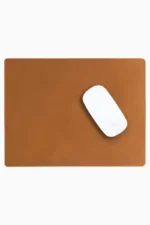 Light brown tan leather mouse pad with tone-on-tone perimeter stitching and rounded corners, with a white wireless mouse placed on the right side, top-down view on a white background.